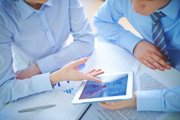 Two employees discussing business document in touchpad at meeting